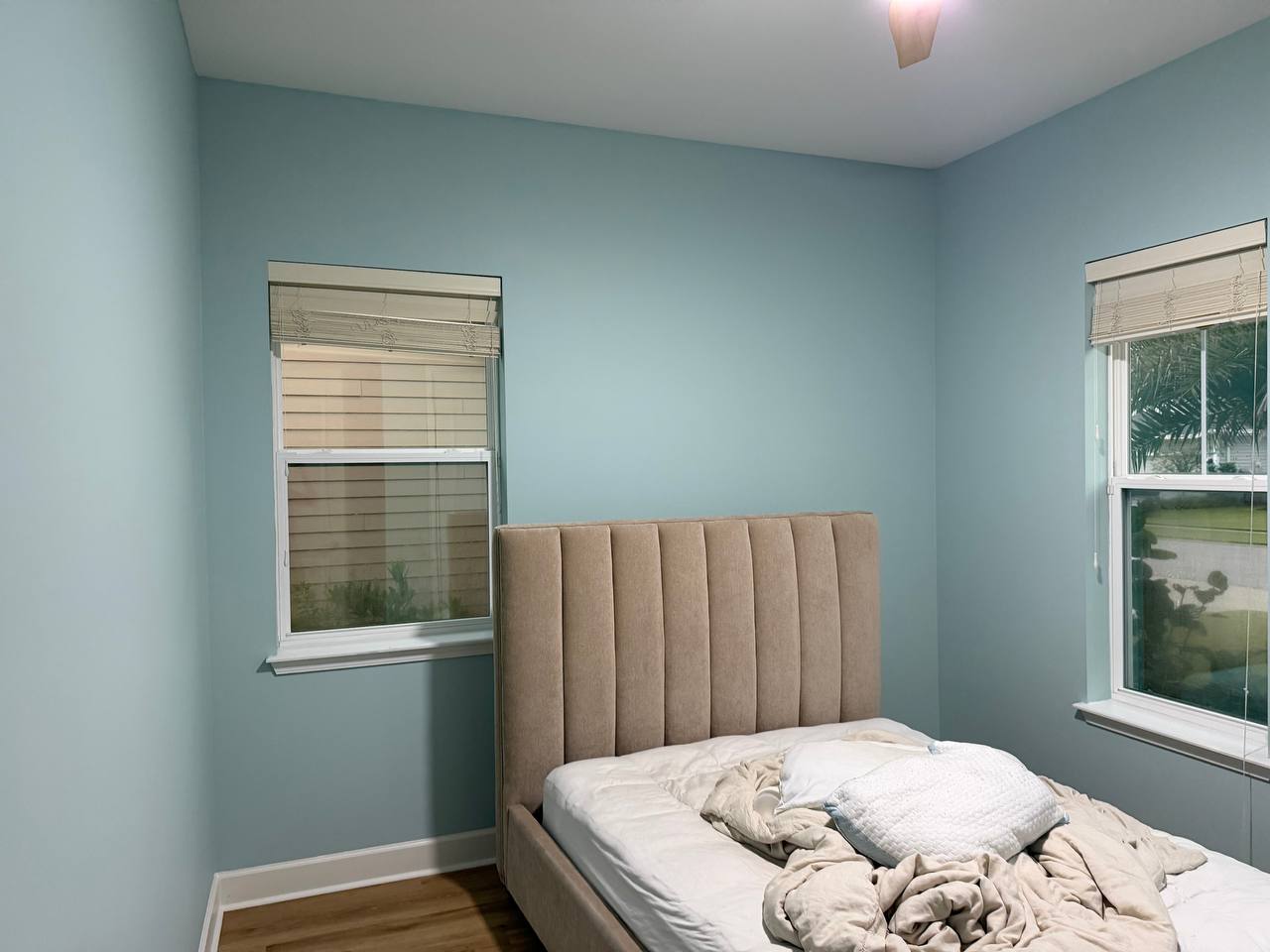 After: bedroom walls painted soft blue-green with crisp white trim, bed and windows uncovered.