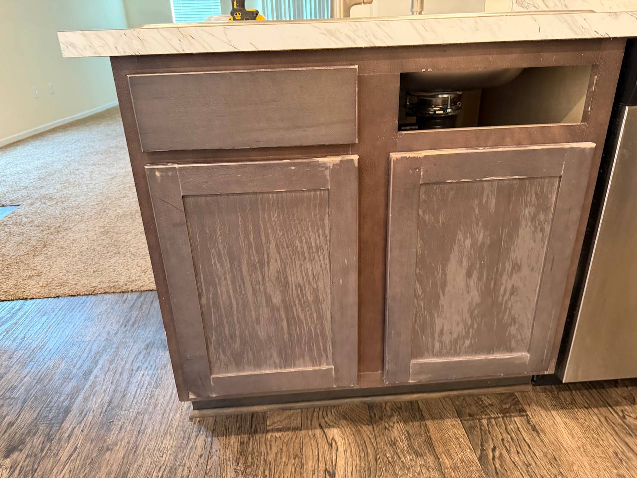 A kitchen sink base cabinet stripped back to bare patches, mid-preparation before priming.
