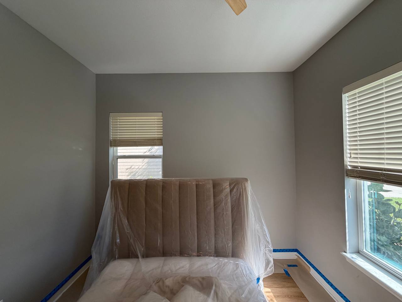 Before: the same bedroom in flat grey, with the bed wrapped in plastic sheeting and blue tape along the baseboards.
