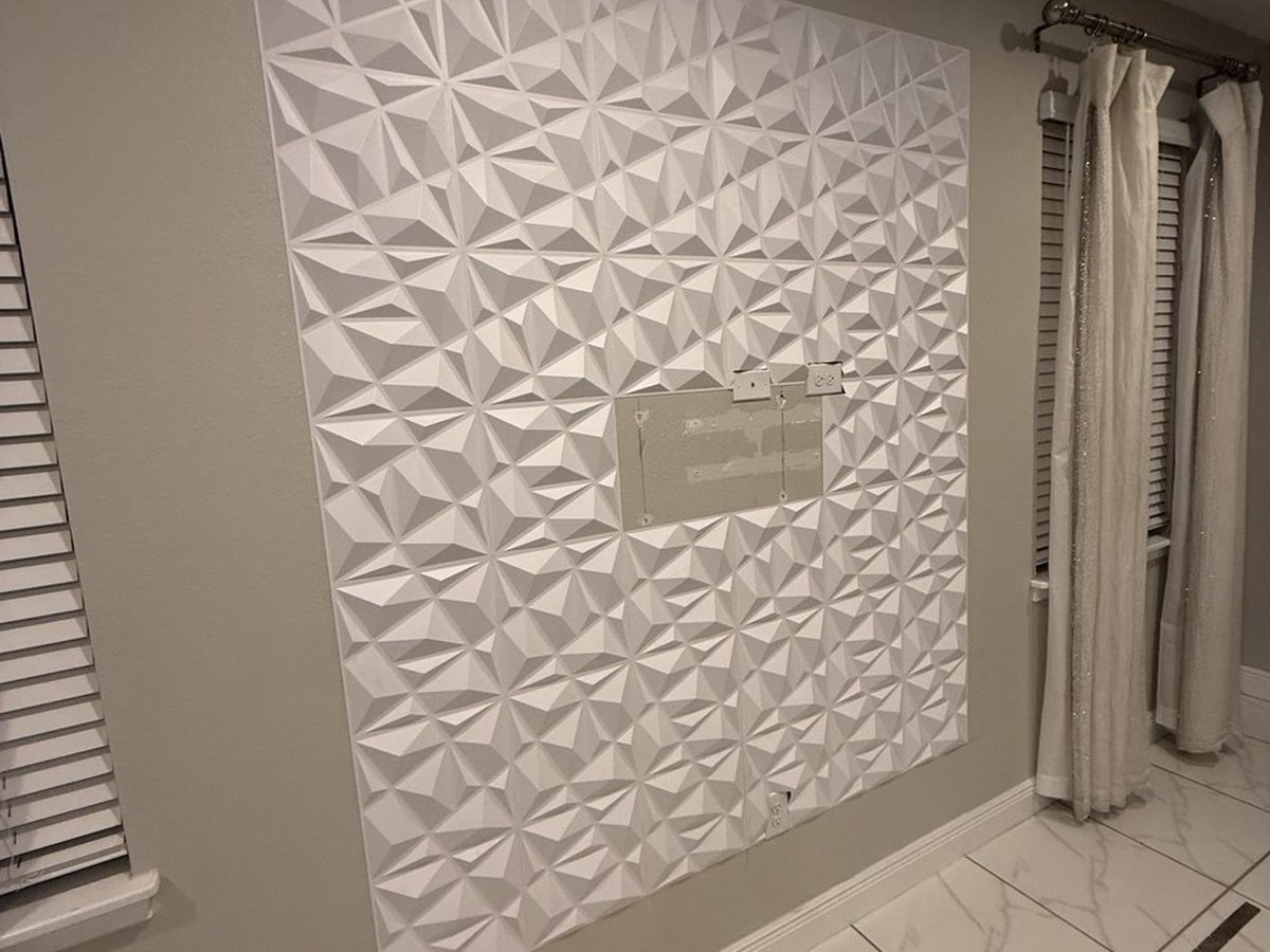 Accent wall covered floor to ceiling in white three-dimensional geometric panels, beside a curtained window.