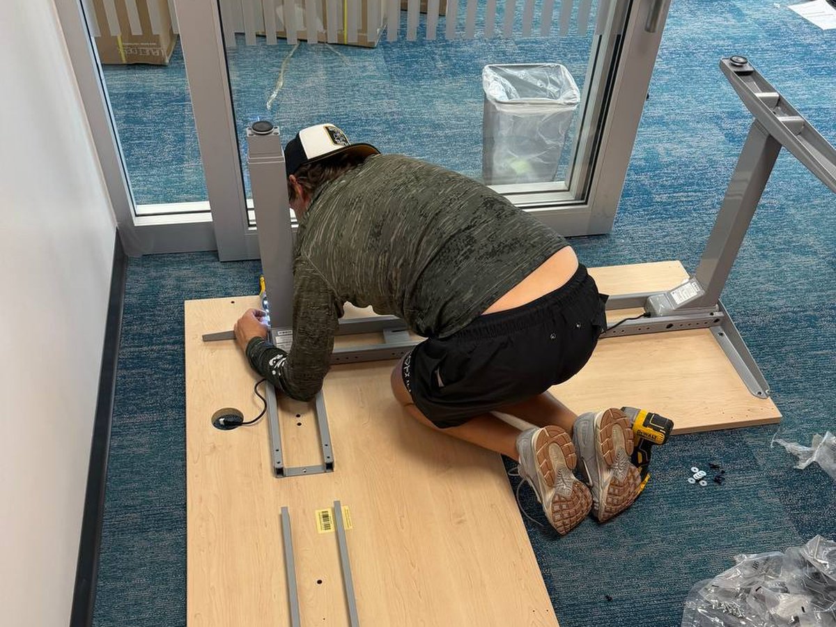 Standing desk being assembled on an office floor, with the desktop and steel frame laid out ready to fit.